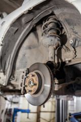 Poster - Disc brake of the vehicle for repair, in process of new tire replacement. Car brake repairing in garage.Suspension of car for maintenance brakes and shock absorber systems. Replacement of brake pads.