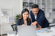 © amnaj - Asian businesswoman and businessman using laptop to discuss and consultation together at meeting. Collaboration of two Asian employees. Two people working in modern office.