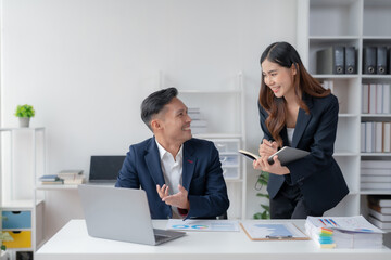 Asian businesswoman and businessman using laptop to discuss and consultation together at meeting. Collaboration of two Asian employees. Two people working in modern office.