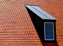 Sloped Red Clay Tile Roof With Round Beaver Tail Edge. Black Metal Plated Roof Dormer With Light Metal Louver. Modern Home Building Materials Concept. Residential Building Construction.