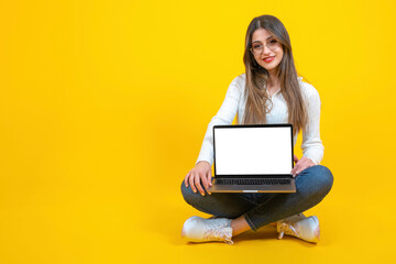 Modern laptop mockup, real caucasian woman sitting ground holding modern laptop mockup. Smiling positive girl showing notebook with empty blank white screen. Yellow background, copy space. 