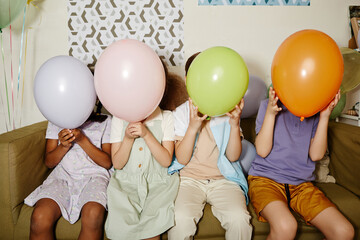 Wall Mural - Diverse group of children holding balloons and hiding faces during party for children shot with flash