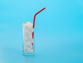 Wall Mural - Glass cup full of sugar cubes on blue background