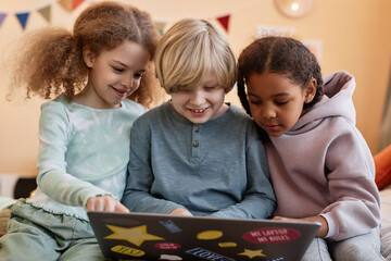 Wall Mural - Group of three little children using laptop together at home and smiling