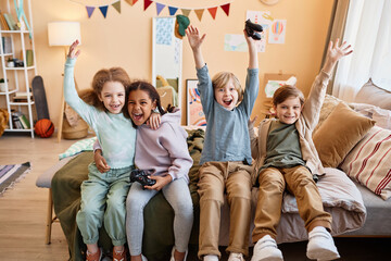 Wall Mural - Diverse group of excited little children playing video games together and cheering