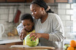 © lordn - Cheerful African-American mother and son in the kitchen preparing a healthy fruit  snack