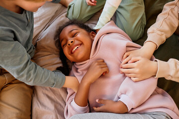 Wall Mural - Diverse group of children playing together and tickling smiling black girl