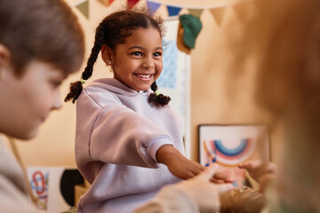 Wall Mural - Portrait of cute black girl playing rock paper scissors with friends while sitting on bed in circle