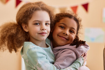 Wall Mural - Portrait of two cute little girls embracing and smiling at camera at home