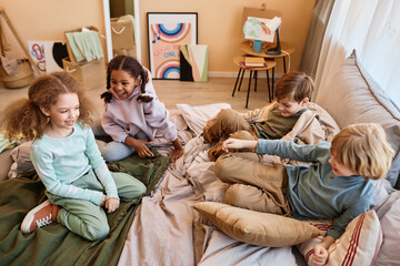 Wall Mural - High angle view at group of happy little children sitting on bed together and chatting