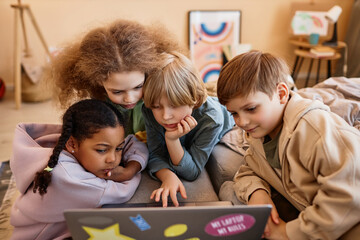 Wall Mural - Group of children looking at computer screen together huddled over laptop