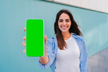 Isolated happy woman showing the green screen of her smartphone. Young smiling female holding a cellphone with chroma key. Mockup of caucasian joyful lady with mobile phone. Template for app or game