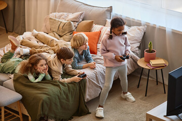 Wall Mural - High angle view at group of children playing videogames together and lying on bed, copy space