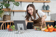 © Natee Meepian - Image of young pretty lady in kitchen and cooking the salad. Looking at tablet computer