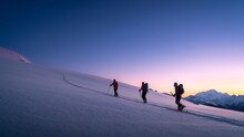 Skiers Touring In Winter, Full Of Snow, At Sunrise Under A Beautfiul Clear Sky Full Of Colors. Living The Dream