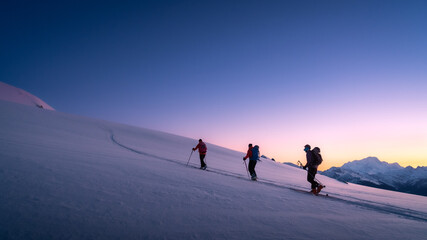 skiers touring in winter, full of snow, at sunrise under a beautfiul clear sky full of colors. livin