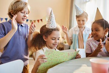 Wall Mural - Diverse group of happy children at Birthday party with cute girl opening presents