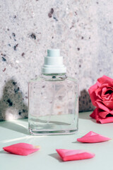 Wall Mural - Glass perfume bottle and coral pink rose flower with petals on natural stone background in sunlight, closeup