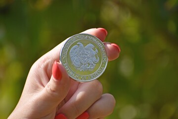 Wall Mural - Close up of a woman's hand holding a coin with the Coat of arms of Armenia on it, blurred background