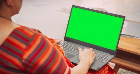 Over-the-Shoulder View of Elderly Indian Woman Using Laptop with Green Screen: Doing Remote Work, Virtual Meetings. Browsing Internet, Doing Online Shopping, Using Software. Template Chroma Key