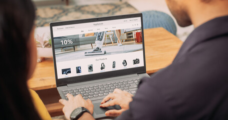 Young Couple Using Laptop to Buy Appliances From the Confort of Their Home: They are Browsing Internet, Doing Online Shopping, Choosing the Best Deal of Sale on Websites, Discussing the Decision 