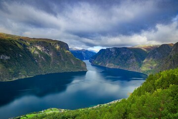 Canvas Print - Aerial view of a blue river surrounded by huge mountains in a rural area in cloudy sky background