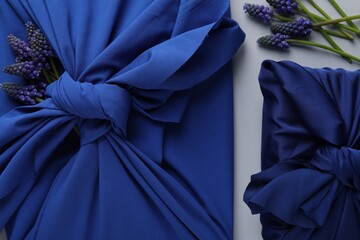 Furoshiki technique. Gifts packed in blue silk fabric and muscari flowers on white table, flat lay