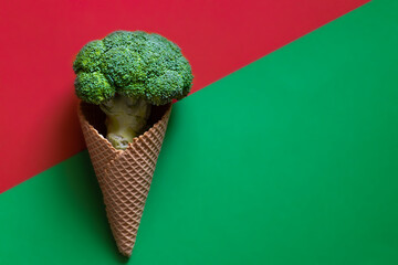 Wall Mural - Broccoli in an ice cream waffle cone on a green and red background. Vegan healthy food concept. Top view, copy space