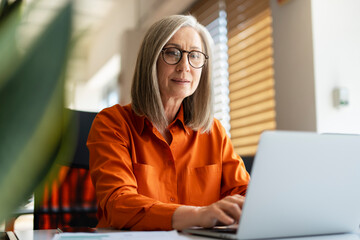 portrait of confident serious mature businesswoman wearing stylish eyeglasses, orange shirt using la
