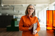 © Maria Vitkovska - Portrait of confident senior businesswoman, CEO wearing stylish eyeglasses, holding laptop computer looking at camera in modern office. Successful business concept