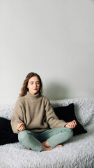 Fototapete - Young woman sitting in lotus position on the sofa with her hands on her knees, meditating, trying to relax her mind and relieve stress