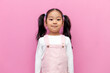 little Asian girl in pink sundress with long hair stands and smiles on pink isolated background