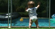 © Marco - Cute infant baby leaning on swimming pool fence watching siblings play inside water