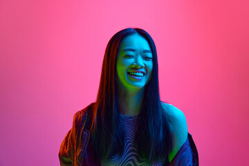 Wall Mural - Portrait of happy, smiling, asian, young girl cheerfully posing against pink studio background in neon light. Happiness, success. Concept of emotions, facial expression, youth, lifestyle, sales, ad