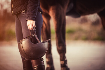 Equestrian girl standing next to her horse and holding her equestrian helmet. Equestrian sport theme.