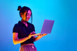 Portrait of young korean girl, student standing with laptop against blue studio background in neon light. Concept of emotions, facial expression, youth, lifestyle, education, business, ad
