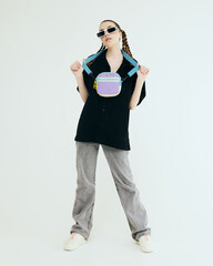 Wall Mural - a stylish teenage girl with a bag poses on a light background in a fashionable summer black shirt and sunglasses