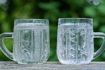 two large white empty crystal mug stand on a gray wooden table in the street on a green background