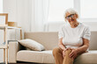 © SHOTPRIME STUDIO - Elderly woman severe pain in her leg sitting on the couch, health problems in old age, poor quality of life. Grandmother with gray hair holds on to her sore knee, problems with joints and ligaments.