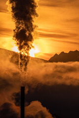 Wall Mural - Smoke from chimny and colorful sky with sun and mountains at background