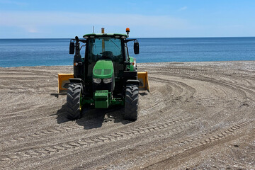 Wall Mural - Tractor with a plow for leveling the surface of the sand on a sandy beach before the opening of the tourist season.