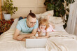 © Kaplitskaya Love - Handsome young man at home with his little cute daughter are lying on the bed with looking into the laptop. Happy Fathers Day.