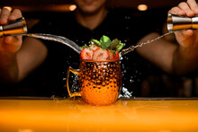 Male Bartender Pours A Jigger Drink Into Cocktail Cup Decorated With Strawberry And Mint Leaves