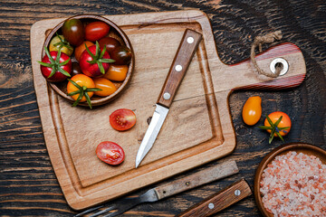 Wall Mural - ripe cherry tomatoes and knife on cutting board. Dark wooden table. View from above.