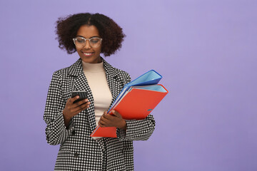 Canvas Print - African American intern with folders using smartphone on purple background. Space for text