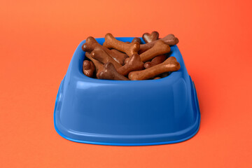 Wall Mural - Blue bowl with bone shaped dog cookies on orange background, closeup