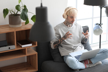 Poster - Young tattooed man in headphones with laptop video chatting at home