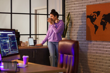 Young female programmer drinking coffee while working in office