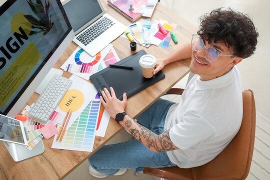 Male graphic designer with cup of coffee working at table in office