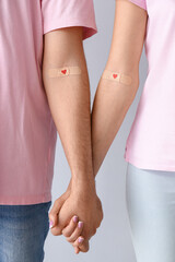 Wall Mural - Young couple after donating blood holding hands on light background, closeup